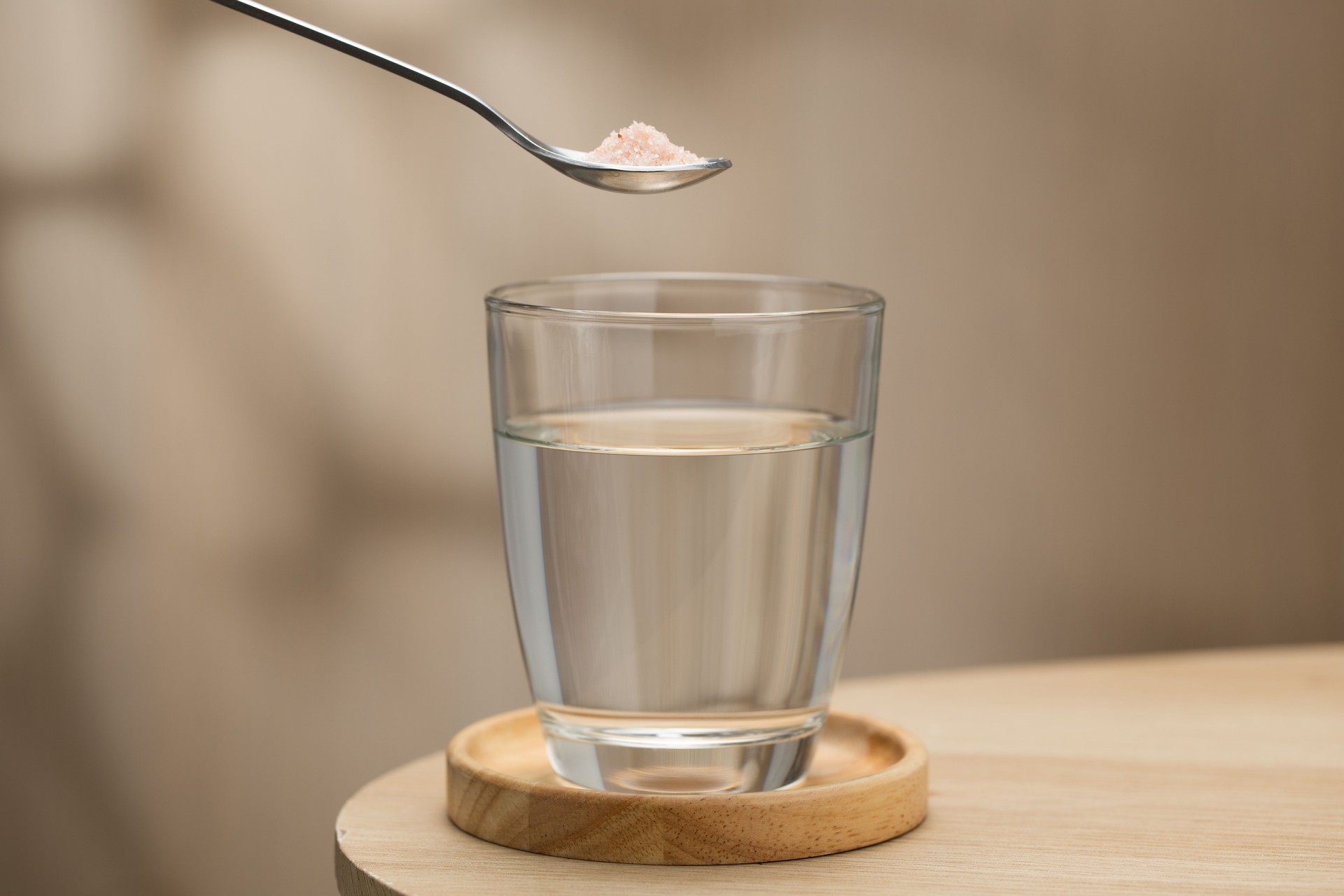 A spoon of Himalayan salt is being added to a glass of drinking water.