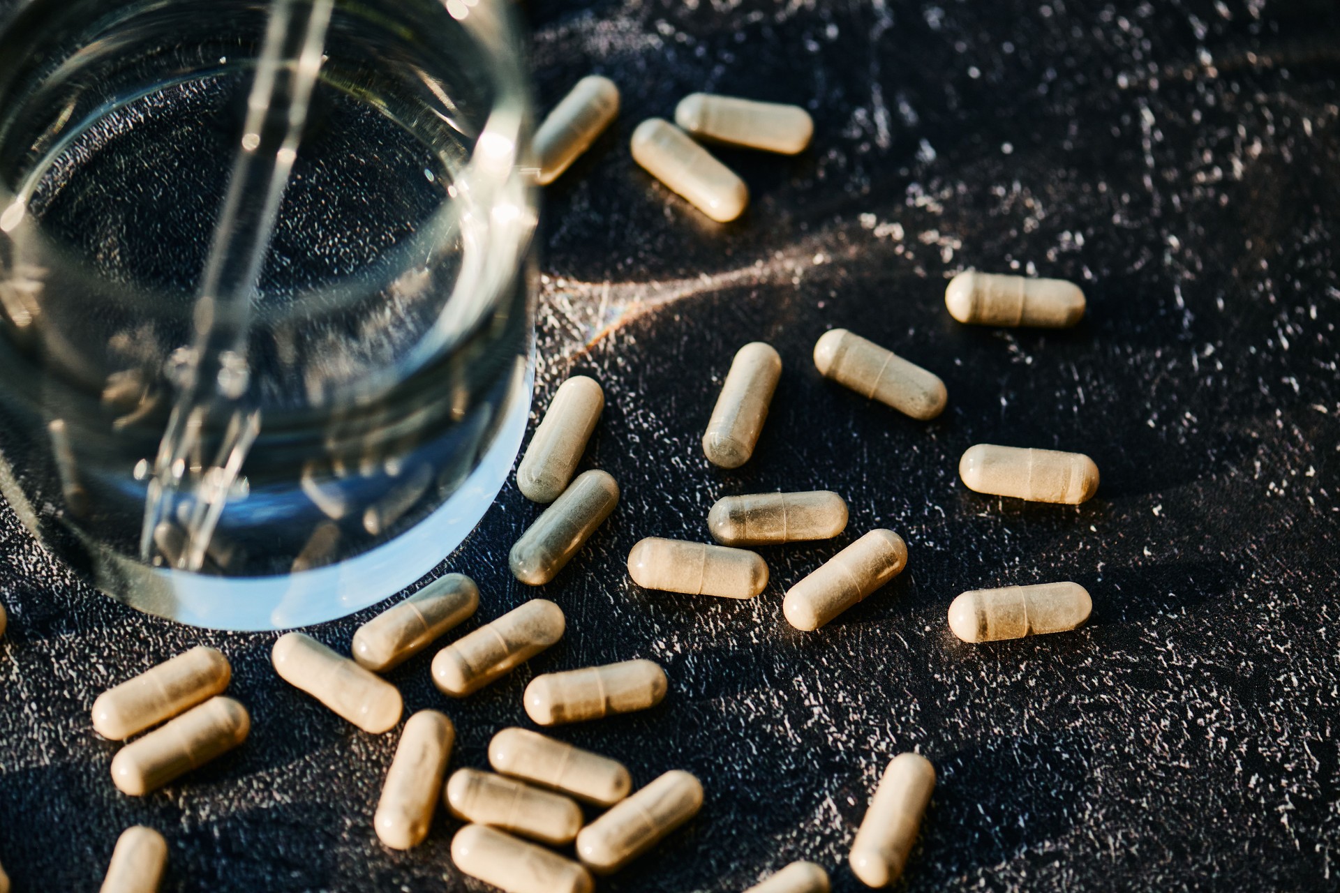 Natural Capsules with Glass of Water on Dark Surface